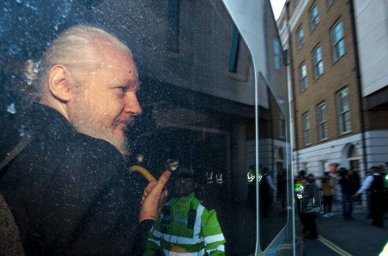 Julian Assange gestures to the media from a police vehicle on his arrival at Westminster Magistrates court on April 11, 2019 in London, England.