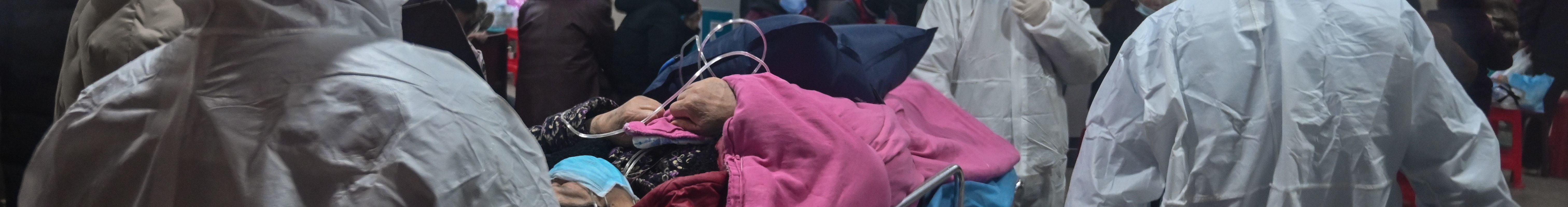 Medical staff wearing full body jumpsuits with hoods, face masks, goggle, gloves, and shoe coverings to protect against a previously unknown coronavirus arrive with a patient on a rolling gurney at the Wuhan Red Cross Hospital in Wuhan on January 25, 2020. The hospital appears crowded from the photo.