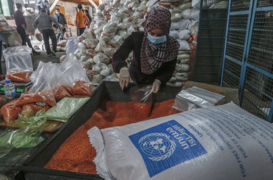 Staff in masks wearing PPE prepare food aid rations to be henceforth delivered to refugee family homes rather than distributed at a UN a center, in Gaza City.