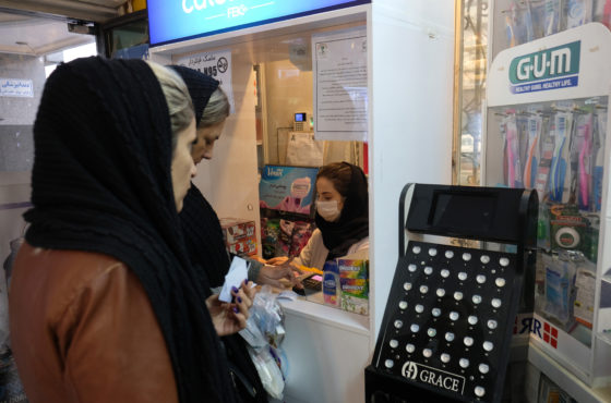 A female cashier wearing a mask to avoid Corona Virus sits behind the till receiving payments from other female customers who are all wearing black veils inside Sadaf pharmacy in Tehran, Iran.