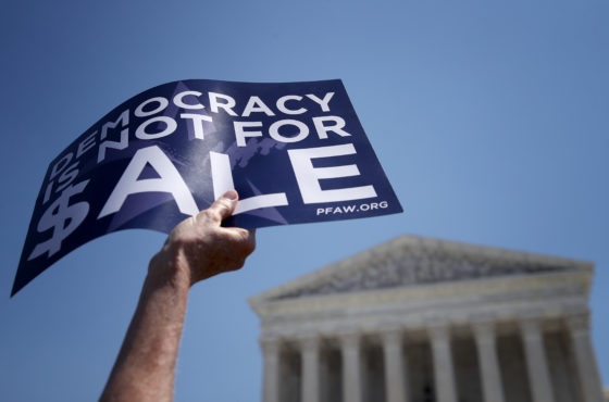 Protesters gather outside the U.S. Supreme Court as Sen. Chuck Schumer (D-NY) speaks during a press conference July 30, 2019 in Washington, DC. A sign reads, "Democracy is not for $ale"