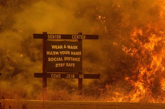 A sign warning people about Covid-19 is surrounded by flames and smoke during the Hennessey fire near Lake Berryessa in Napa, California on August 18, 2020.