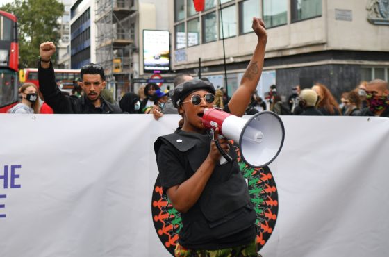 People gather in Westbourne Park to take part in the inaugural Million People March from Notting Hill to Hyde Park in London on August 30, 2020, to put pressure on the UK Government to address the UK's institutional and systemic racism. A banner reads, “Taking the initiative party” and “Racism is uncivilized.”