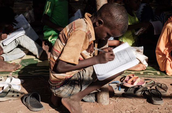 Ethiopian refugee grade four pupils who fled the Tigray conflict attend class at a makeshift classroom set by the Norwegian Refugee Council (NRC) at Um Raquba refugee camp in Gedaref, eastern Sudan, on December 7, 2020. One child squats on the ground surrounded by shoes while the others sit on a blanket. The children hold books and papers in their laps.