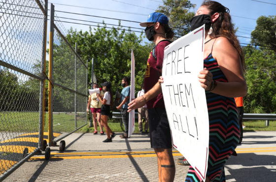 Activists stand at the entry gate to the Krome Service Processing Center as they honor the life of Kuan Hui Lee, who died in the custody of ICE at the Krome Service Processing Center. One sign reads, “Free them all.” They wear facemasks. August 15, 2020 in Miami, Florida