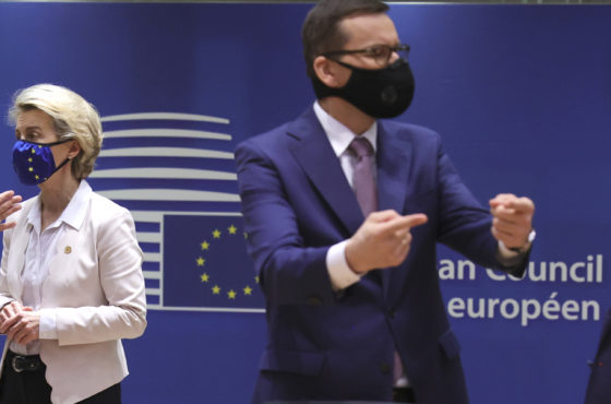French President Emmanuel Macron speaks with European Commission President Ursula von der Leyen as Hungary's Prime Minister Viktor Orban speaks with Poland's Prime Minister Mateusz Morawiecki during a round table meeting during an EU summit at the European Council building in Brussels, on December 10, 2020. They stand talking, not actually sitting at the table. They all wear face masks. Behind them a wall is covered with a banner reading “European Council.”