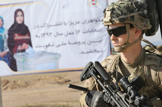 Sargent Forrest Huckabey from Neodesha, Kansas with the U.S. Army's 2nd Battalion 87th Infantry Regiment, 3rd Brigade Combat Team, 10th Mountain Division stands guard with a gun in front of a billboard which encourages women to vote in Afghanistan's April 5th presidential election during a patrol outside of Forward Operating Base (FOB) Shank on March 29, 2014 near Pul-e Alam, Afghanistan.