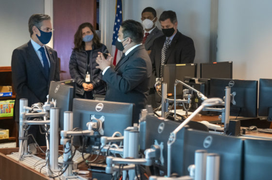 Secretary Blinken Visits the State Department's Diplomatic Security Service Command Center. People wear face masks as they stand near desks with five to seven computer screens in semicircles.