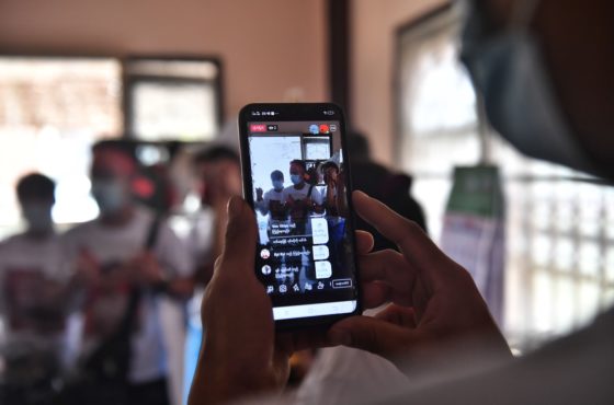 Myanmar migrants share their activities on social media before going to a local protest against the military coup in their home country, at a house in the outskirts of Bangkok on February 7, 2021. One person holds a phone recording the others. They wear face masks.