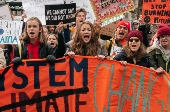 Demonstrators from several environmental groups including Extinction Rebellion and Sunrise Movement demand broad action at a youth-led climate strike near City Hall on December 6, 2019 in New York City. A large banner reads, “Climate Change” but “Climate” is crossed-out and “System” is written in its place to read “System Change.” Youth carry additional signs reading, “Respect your mama” with an Earth symbol; “We cannot say we did not know;” “Hey Exxon, stop burning my future;” “No more excuses;” and more.