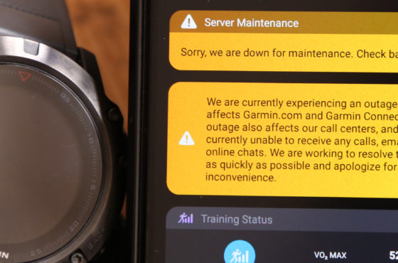 A phone show the Garmin Connect software with an error message that reads, “Server Maintenance: Sorry, we are down for maintenance. Check back shortly.” and “We are currently experiencing an outage that affects Garmin.com and Garmin Connect. This outage also affects our call centers, and we are currently unable to receive any calls, emails, or online chats. We are working to resolve this issue as quickly as possible and apologize for this inconvenience.” A watch that is clearly not working and has a dark screen is shown next to the phone with these messages.
