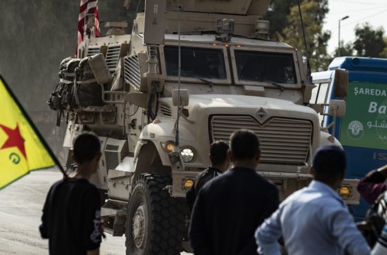 Syrian Kurds, one of them carrying a Kurdish YPG (People's Protection Units) flag, watch as a US military vehicle drives on a road after US forces pulled out of their base in the Northern Syrian town of Tal Tamr, on October 20, 2019.