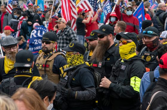 Members of the Proud Boys join supporters of US President Donald Trump as they demonstrate in Washington, DC, on December 12, 2020. They dress in black and yellow with bullet-proof vests. A few wear masks but the majority do not. Trump supporters in the background waive American flags and Trump banners. A few wear face masks but many do not.