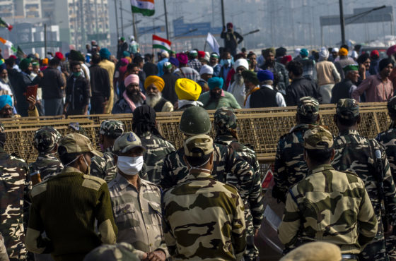 Farmers in India protest against new harmful farming laws while Indian paramilitary soldiers watch them behind barricades on December 13, 2020 at the Delhi-Uttar Pradesh border in Ghaziabad, India.