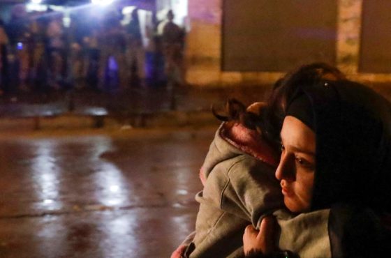 A woman crosses a street with her child during clashes between security forces and anti-government protesters in the northern city of Tripoli, on January 29, 2021.