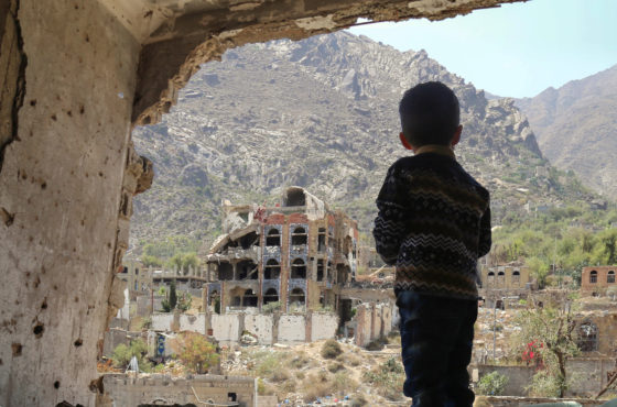 A Yemeni child standing under a damaged building looks out of a missing wall at buildings that were heavily damaged in an air strike in the southern Yemeni city of Taez.