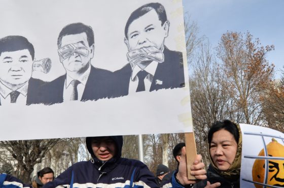 Protestors hold posters during an anti-corruption rally in Bishkek on December 18, 2019. A poster shows an three images of an official with money in ears, over the eyes, and stuck in his mouth.
