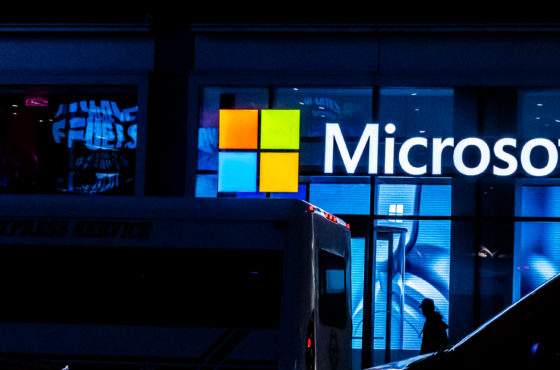A bus passes a large Microsoft sign and logo lit up in bright lights.
