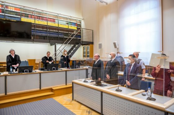 People gather in the courtroom waiting to hear the verdict to Syrian defendant Eyad al-Gharib on February 24, 2021 in Koblenz, western Germany. Some people wear masks, but not all. Clear barriers are set up around each desk station.