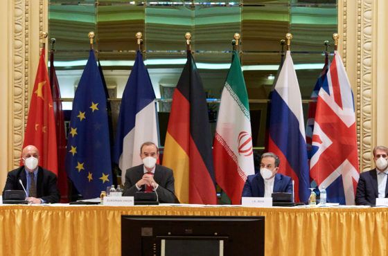 Representatives of the European Union and Iran sit at a table attending the Iran nuclear talks at the Grand Hotel on April 06, 2021 in Vienna, Austria. Flags stand behind the representatives. They wear face masks and sit mostly socially distanced.
