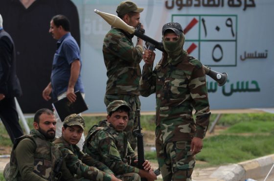 Iraqi fighters of the Hashed al-Shaabi units stand guard during a campaign gathering for the Fateh Alliance, a coalition of Iranian-supported militia groups, in Baghdad on May 7, 2018, ahead of Iraq's parliamentary elections to be held on May 12. Some hold weapons, and a few sit on the ground.