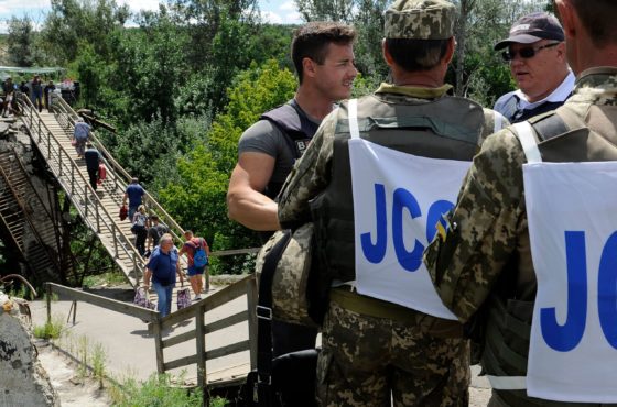 Ukrainian officers of the Joint Centre for Control and Coordination (JCCC) and OSCE employees watch as people walk across a destroyed bridge between the Ukraine-controlled territory and territory held by Russia-backed separatists at a checkpoint near the village of Stanytsia Luhanska, in Luhansk region, eastern Ukraine on August 1, 2019.
