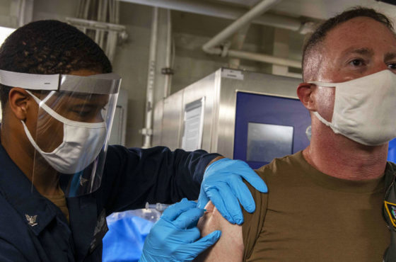 Hospital Corpsman 3rd Class Hizyme Potter, administers a COVID-19 vaccine to Capt. Stewart Bateshansky, commodore of Amphibious Squadron (PHIBRON) 3, aboard the amphibious assault ship USS Makin Island (LHD 8) in the Arabian Gulf, March 19, 2021. Both wear face masks and Hospital Corpsman Potter wears gloves and a face shield.